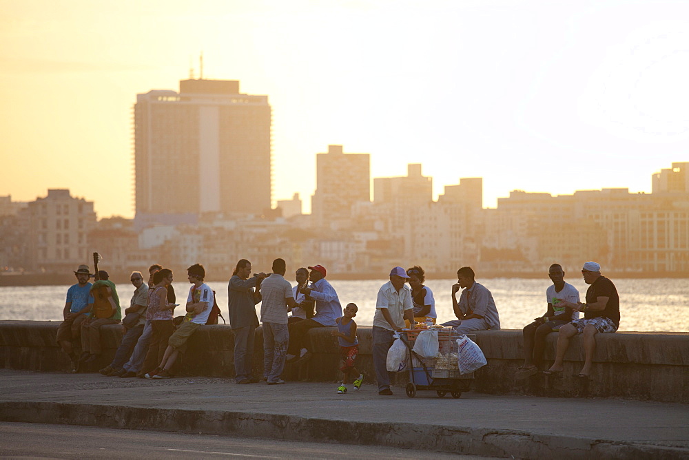 Local people sat on the sea wall at sunset, with buildings of Havana in the background, The Malecon, Havana Centro, Havana, Cuba, West Indies, Central America