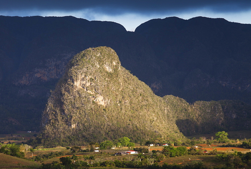 View across Vinales Valley, UNESCO World Heritage Site, from Hotel Los Jasmines in stormy weather showing one of the limestone Magotes lit by the sun against mountains in shade, Vinales, Pinar Del Rio Province, Cuba, West Indies, Central America  