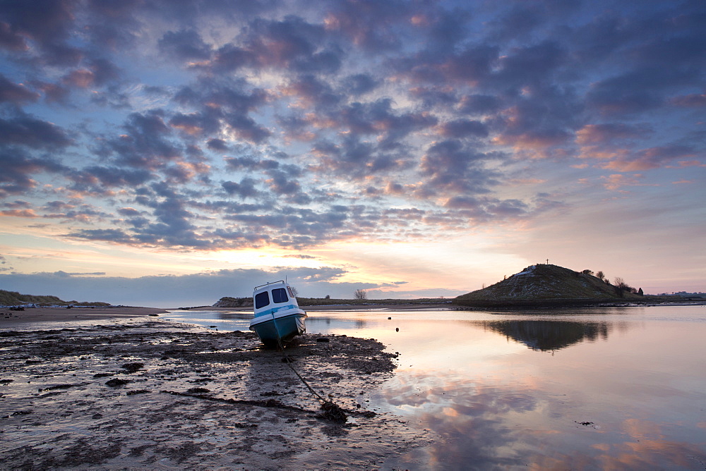 Winter sunrise on the Aln Estuary with a single boat moored on the mud flats, looking towards Church Hill reflecting in the calm water, Alnmouth, near Alnwick, Northumberland, England, United Kingdom, Europe 