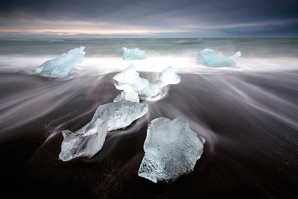 Glassy pieces of ice on volcanic black sand beach with blurred waves, near Jokulsarlon Lagoon, South Iceland, Polar Regions