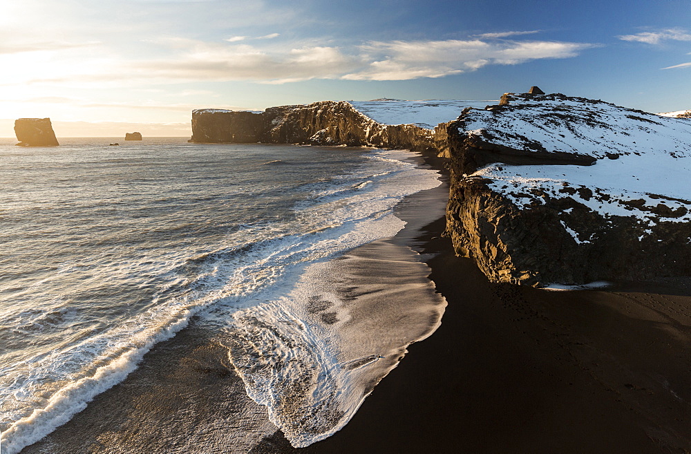 Winter view towards snow covered headland at Dyrholaey bathed in evening sunlight, near Vik, South Iceland, Polar Regions