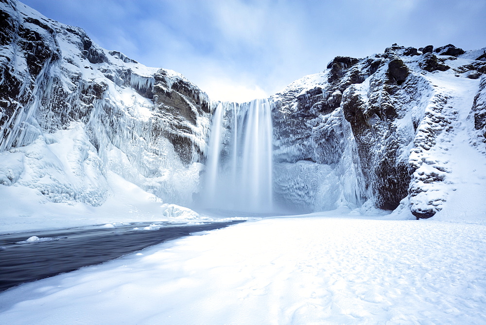 Winter view of Skogafoss waterfall, with cliffs covered in icicles and foregreound covered in snow, Skogar, South Iceland, Polar Regions