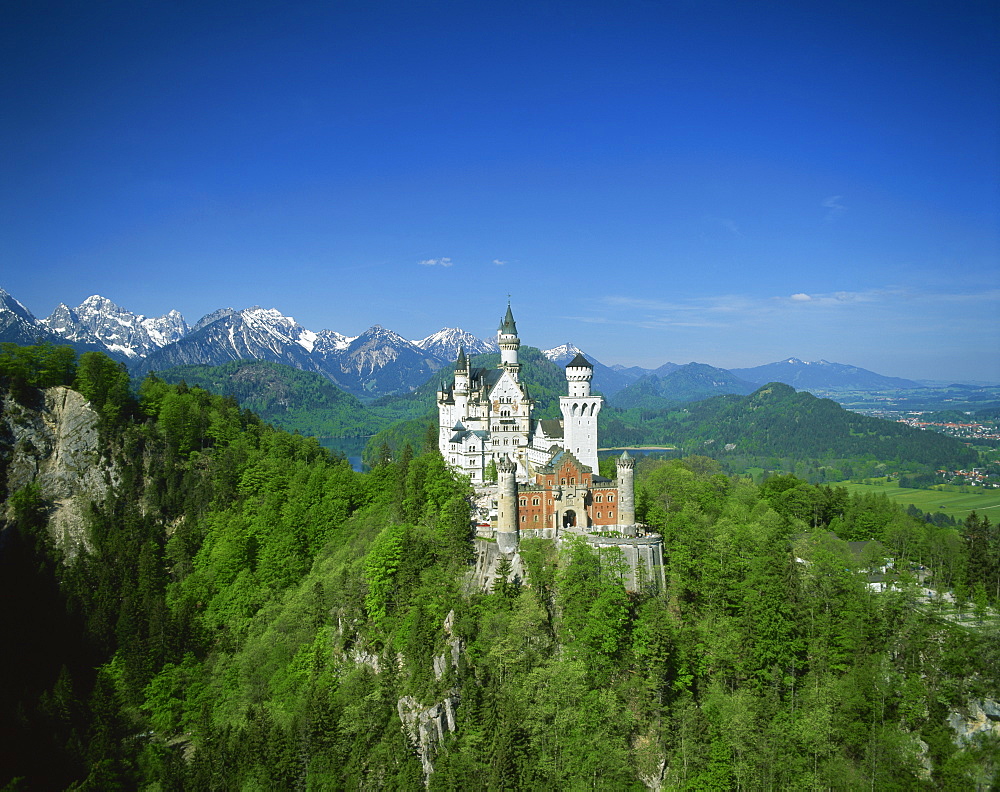 The Neuschwanstein Castle on a wooded hill with mountains in the background, in Bavaria, Germany, Europe