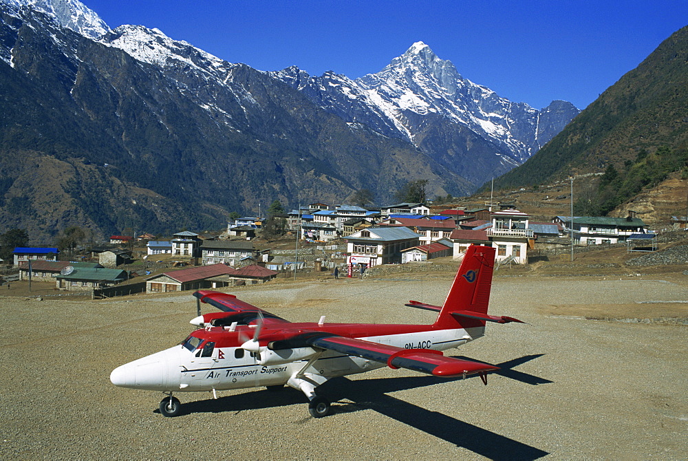 Small propellor aeroplane on the airstrip at Lukla, with village and mountains in the background, in the Himalayas, Nepal, Asia