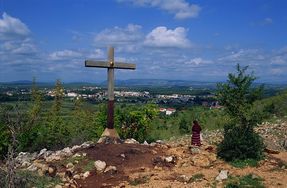 Cross and pilgrim on Apparition Hill, with town beyond, Medjugorje, Bosnia Herzegovina, Europe