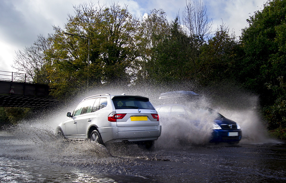 Vehicles splash through flood water on public road, London, England, United Kingdom, Europe