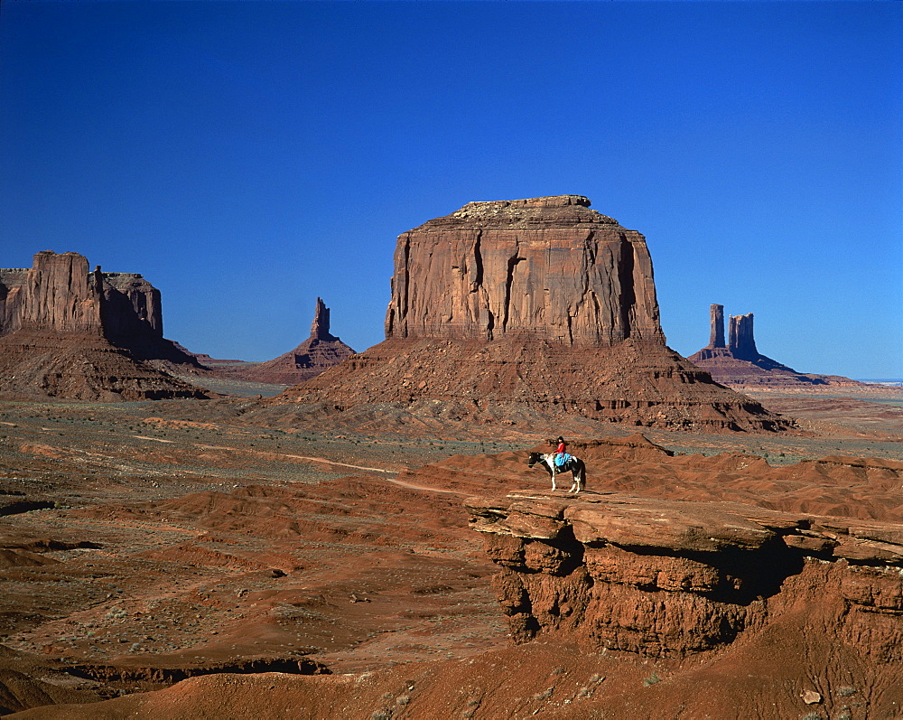 A woman on horseback in the desert with rock formations caused by erosion in the background, in Monument Valley, Arizona, United States of America, North America