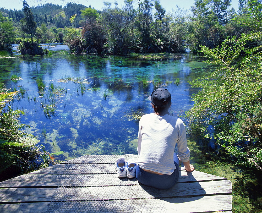 A tourist sitting on the edge of Pupu springs, largest freshwater spring in New Zealand, at Golden Bay, South Island, New Zealand, Pacific