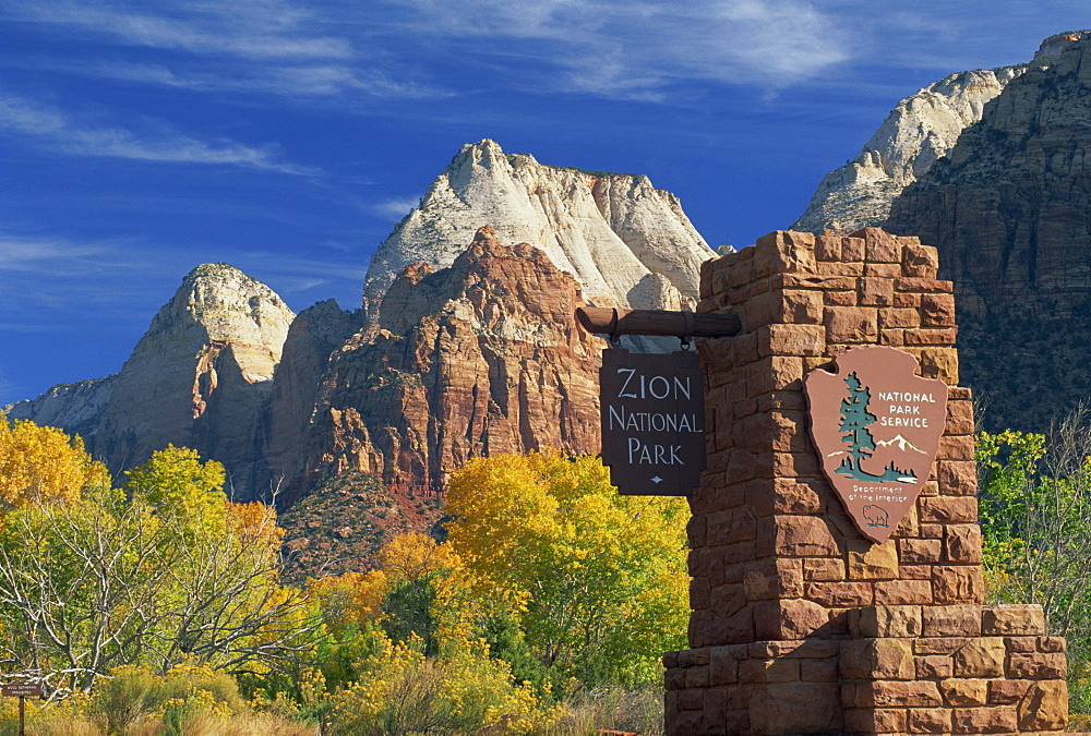 Sign at south entrance to the Park, trees in fall colours, and the Mountain of the Sun and the Twin Brothers peaks, in the Zion National Park, Utah, United States of America, North America