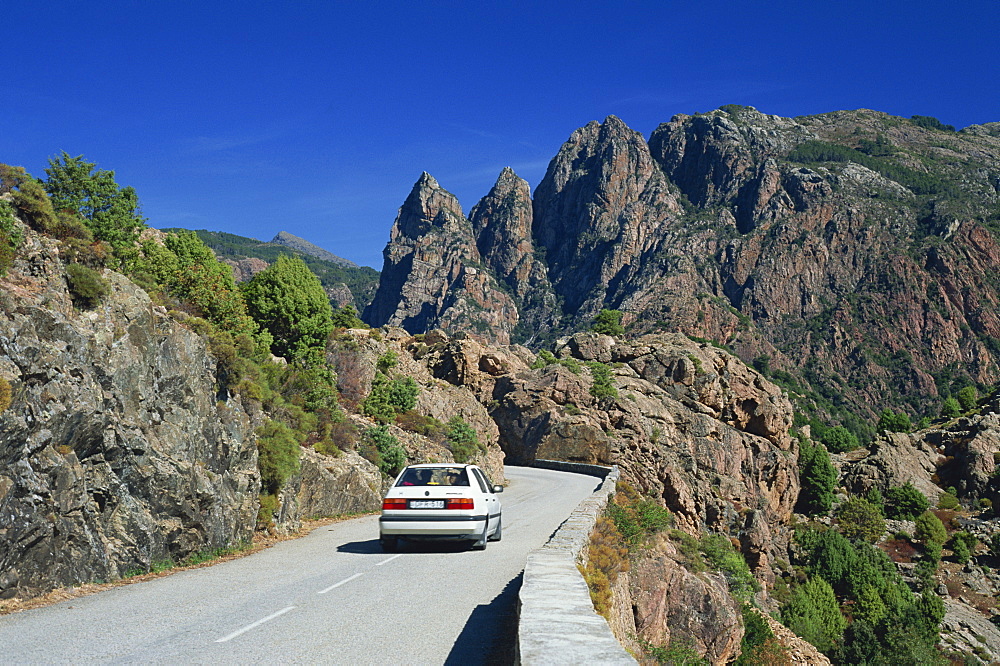 Car on mountain road above the Spelunca Gorge, with Capo Ferolata behind, near Porto, Corsica, France, Europe