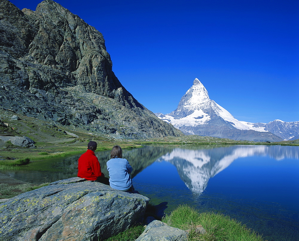 Hikers on rock, the Matterhorn reflected in the Riffelsee, near Rotenboden, Zermatt, Valais, Switzerland, Europe