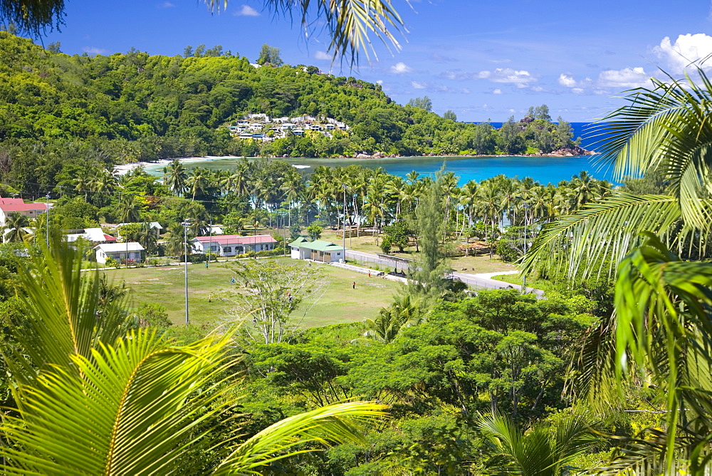 View from hillside across playing field to village and bay, Baie Lazare, Baie Lazare district, Island of Mahe, Seychelles, Indian Ocean, Africa