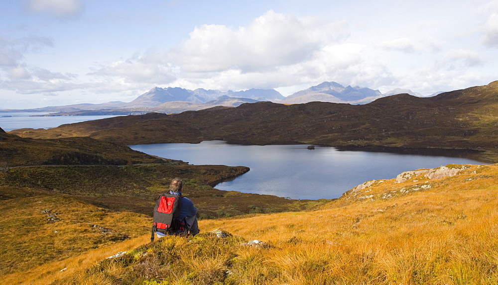 Hiker looking across Loch Dhughaill towards the distant Cuillin Hills, Sleat Peninsula, near Tarskavaig, Isle of Skye, Highland, Scotland, United Kingdom, Europe