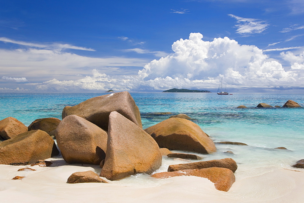 Granite boulders on the shore at Anse Lazio, island of Aride visible on horizon, Baie Sainte Anne district, Island of Praslin, Seychelles, Indian Ocean, Africa