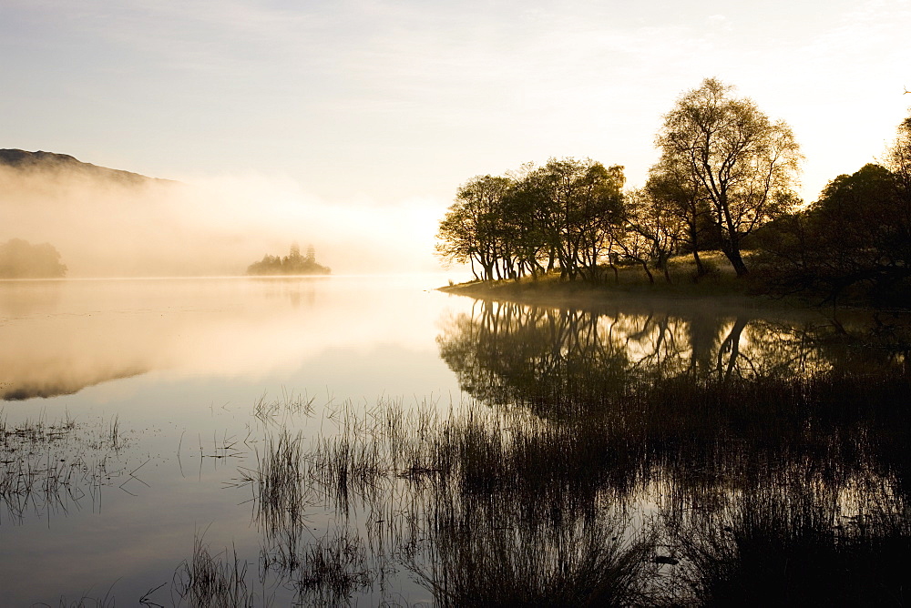 Early morning mist reflected in the still waters of Loch Achray, near Aberfoyle, Loch Lomond and the Trossachs National Park, Stirling, Scotland, United Kingdom, Europe