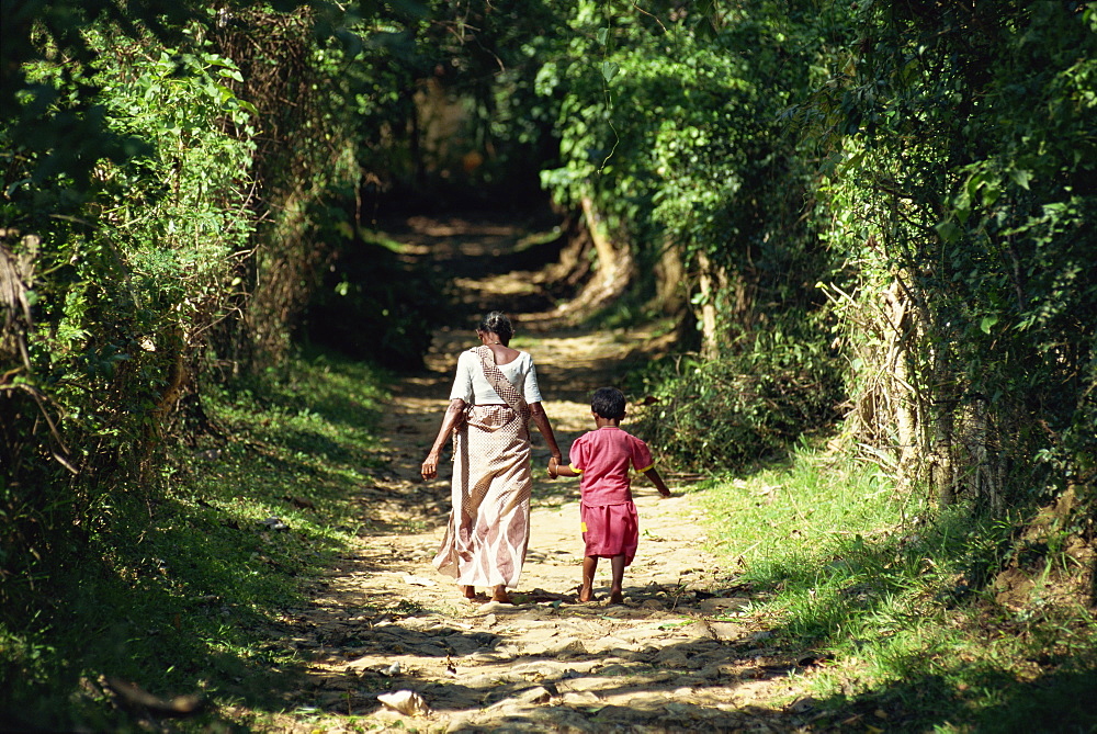 Grandmother and child walking up leafy avenue near Dambulla, Sri Lanka, Asia