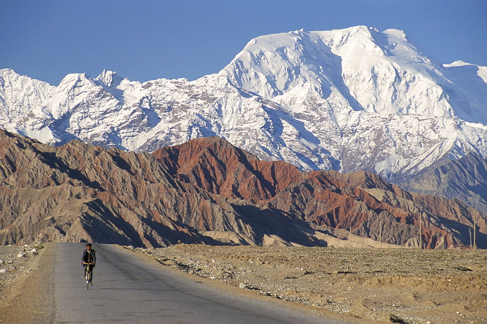 Cyclist on road below mountains, near Lake Kara Kul, Xinjiang, China, Asia