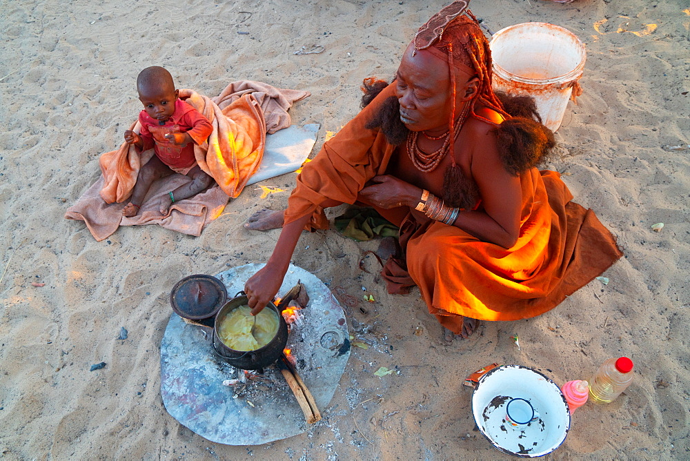 One senior red ochred Himba woman with her child cooking on an open fire, Puros Village, nearr Sesfontein, Namibia, Africa