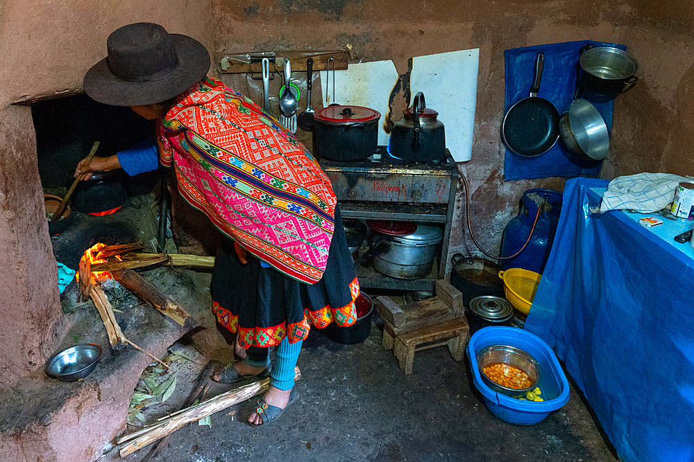 Local woman in colourful traditional dress cooks breakfast over an open fire, Chumbe Community, Lamay, Sacred Valley, Peru, South America