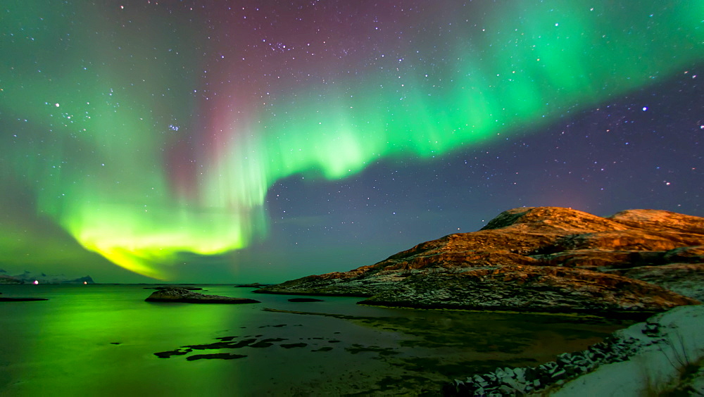 Pink and green aurora borealis (Northern Lights) photographed reflected in the sea near Tromso, Norway, Scandinavia, Europe