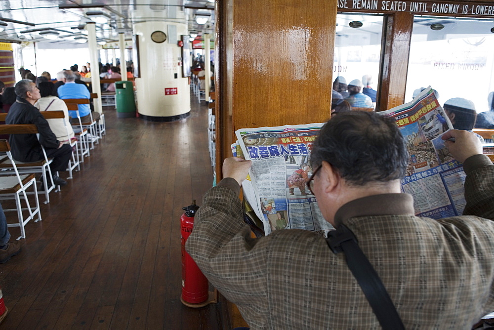 Back view of a man reading a Chinese newspaper onboard a Star Ferry, Hong Kong, China, Asia