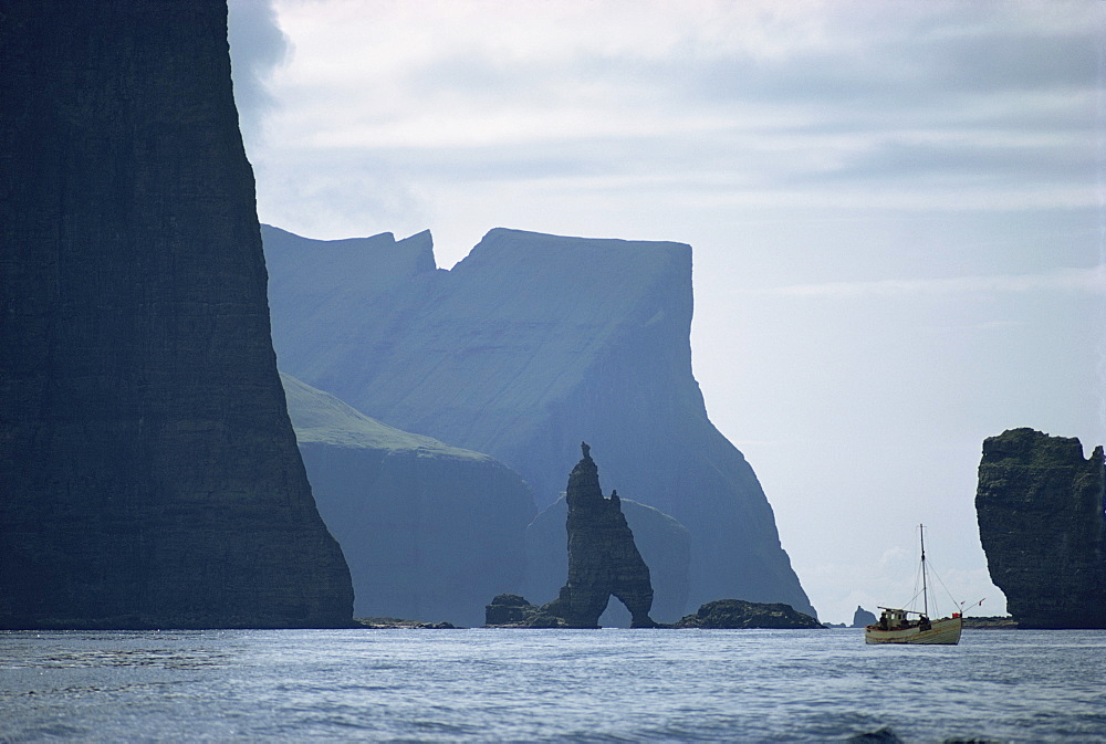 Small fishing boat before a towering cliff coastline, Faroe Islands, Denmark, Atlantic, Europe