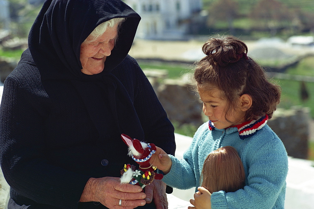 Portrait of an old lady in black giving a toy to a girl on the island of Ios, Cyclades, Greek Islands, Greece, Europe