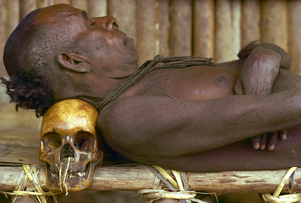 An Asmat man sleeping with his head resting on a skull in Papua New Guinea, Pacific