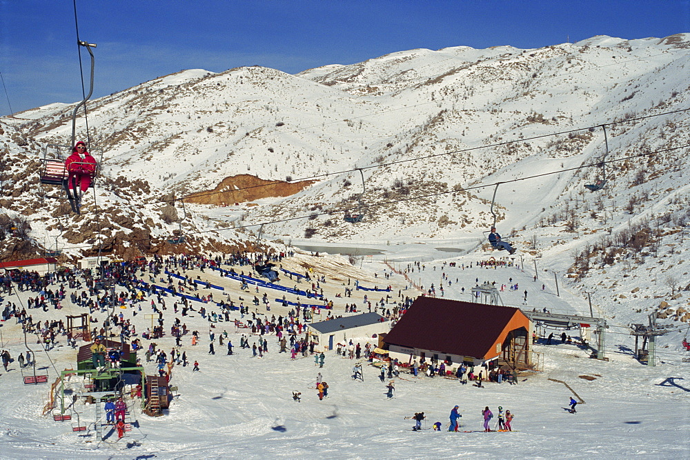 Woman on chairlift above crowds of skiers and tourists at the Neve Ativ Ski Resort on Mount Hermon, Israel, Middle East