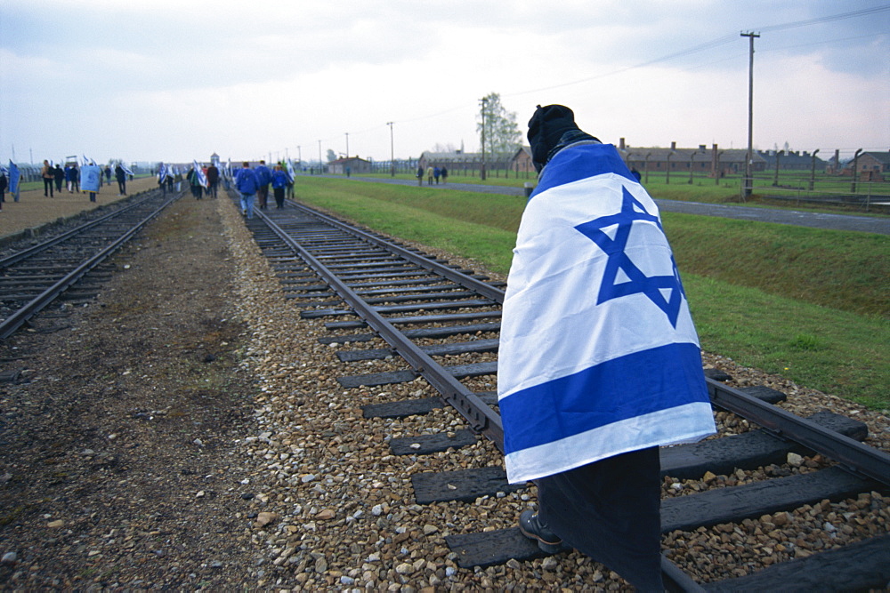 Youngster wrapped in flag walking on rail, Birkenau Concentration Camp, Oswiecim, Malopolska, Poland, Europe