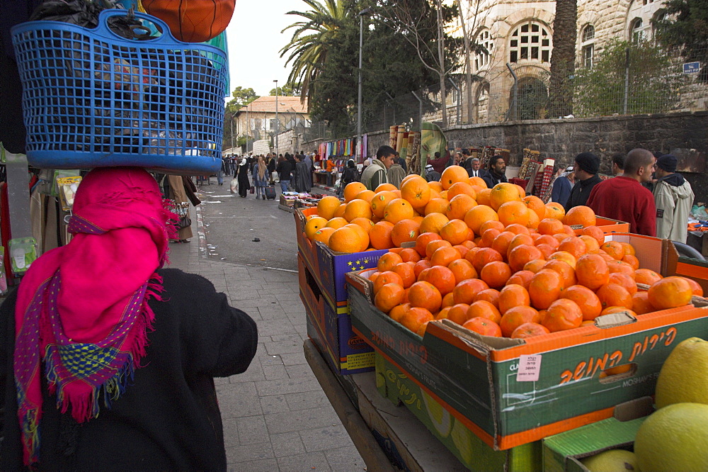 Palestinian woman in colourful scarf and carrying bag on her head walking past an orange stall, Damascus Gate area, Jerusalem, Israel, Middle East