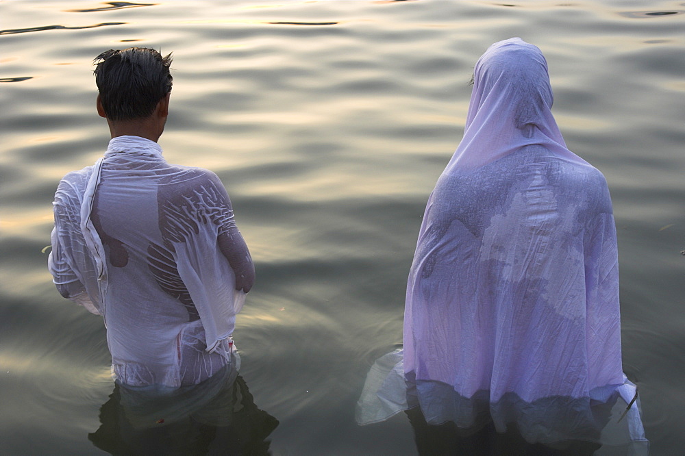 Two pilgrims in white dress making Puja celebration in the Pichola Lake at sunset, Udaipur, Rajasthan state, India, Asia