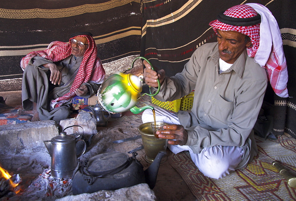 Bedouin man wearing keffiyah pouring tea in Bedouin camp, Wadi Rum, Jordan, Middle East