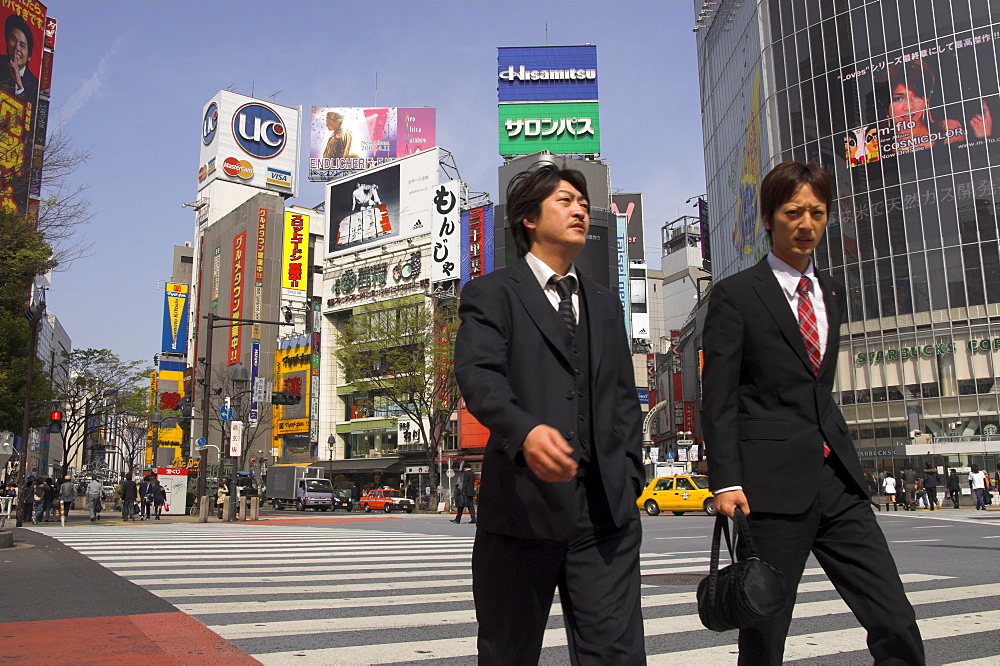 Two well dressed young men walking on zebra crossing with advertising posters and huge video screen in background, Shibuya, Tokyo, Honshu, Japan, Asia