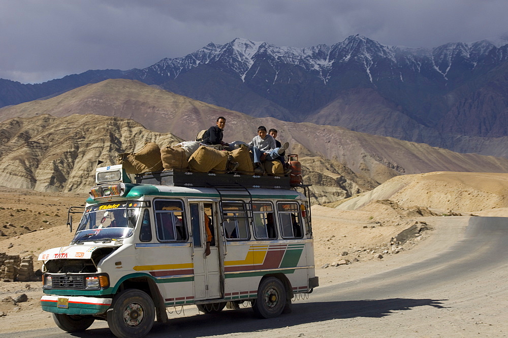 Loaded mini bus with half open engine lid and people sitting on the roof top on the road between Leh and Alchi, Indus Valley, Ladakh, India, Asia