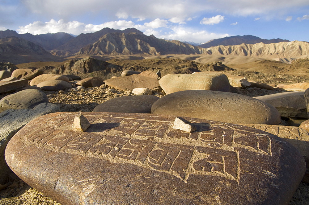 Close up of traditional carved prayer stones on a prayer wall with desert landscape and mountains beyond, Alchi, Ladakh, India, Asia