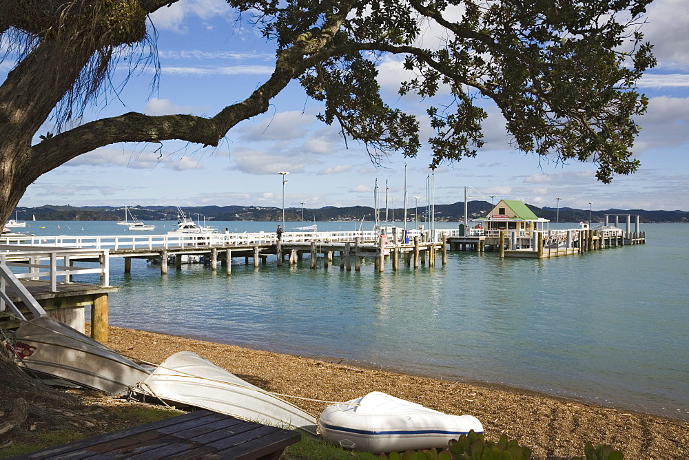 Upturned boats on beach with pier to wharf in bay framed by Pohutukawa tree branches, Russell, Bay of Islands, Northland, North Island, New Zealand, Pacific