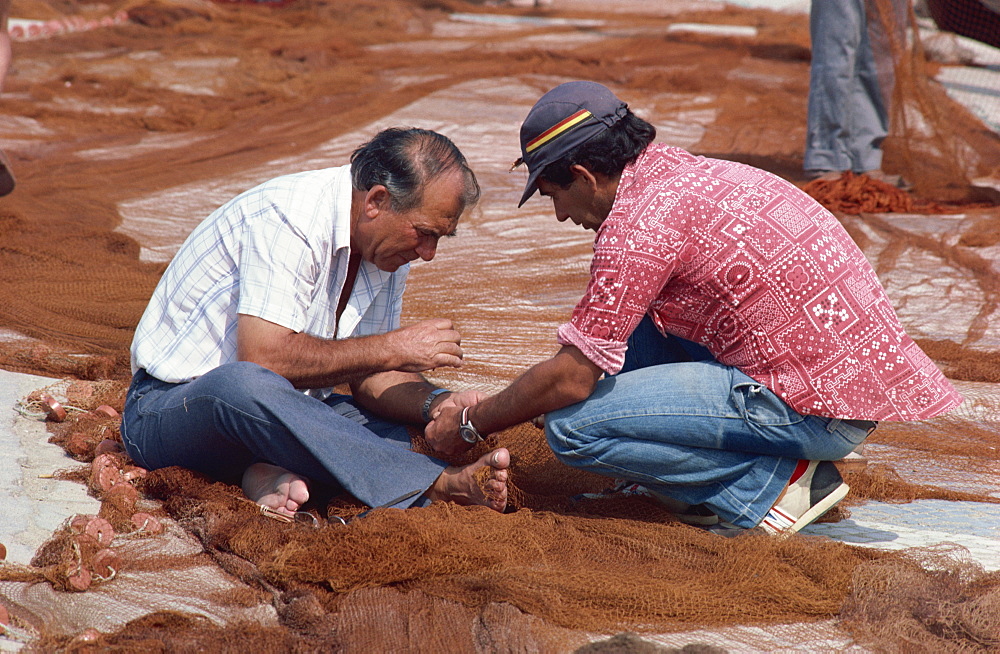 Fishermen mending nets on quayside, Nazare, Portugal, Europe