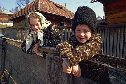 Portrait of two children on a cart, the girl in a head scarf, the boy in a tall woollen hat, smiling and looking at the camera, at Bottiza Village, Romania, Europe