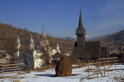 Haystack in snow covered field with two churches in the background at Botita village, Maramures, Romania, Europe