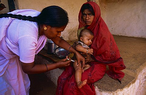 Portrait of an Indian mother holding her baby whilst the child receives a vaccination from an aid project worker, Bangalore, India, Asia