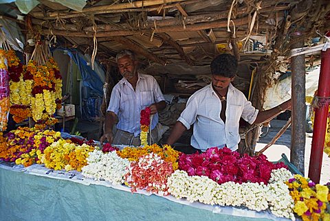 Two men selling flowers and garlands off a stall in the market in a small town in the Western Ghats, Munnar, Kerala, India, Asia