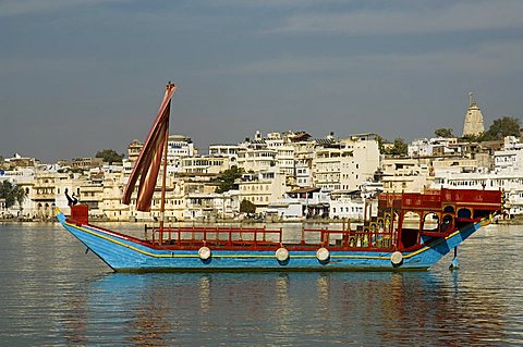 Ceremonial boat used by the Lake Palace Hotel with city of Udaipur in the background, Rajasthan state, India, Asia