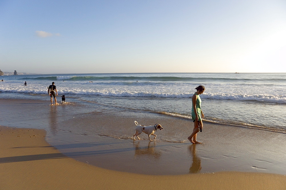 A young woman walks her dog at Arrifana beach, Algarve, Portugal, Europe