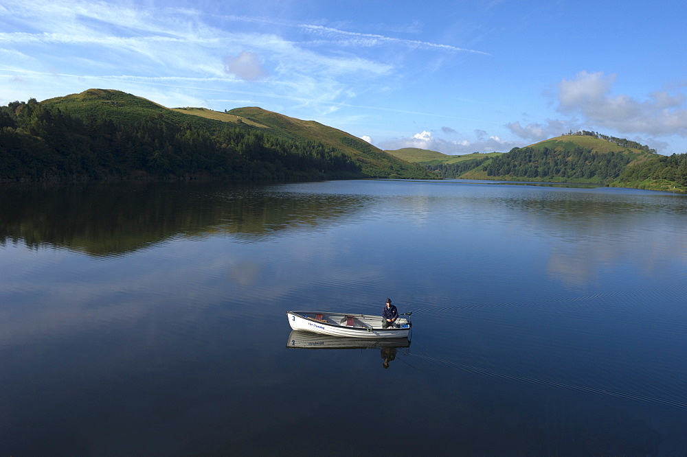 A man fishing from a boat at Llyn (Lake) Clywedog, Llanidloes, Powys, Wales, United Kingdom, Europe