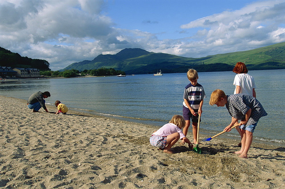 A small group of children digging on the beach by the lake, Loch Lomond, Trossachs, Scotland, United Kingdom, Europe