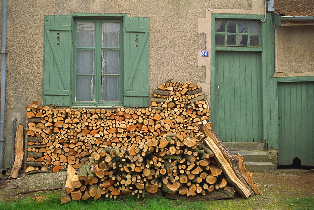 Logs piled outside a traditional cottage with shutters at the window, at Meuse, Alsace Lorraine, France, Europe