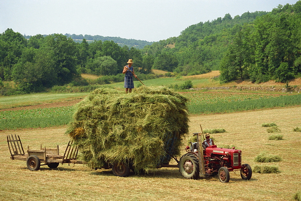 Farming couple with tractor and full trailer during haymaking in a field near Lalbenque, Lot, Midi Pyrenees, France, Europe