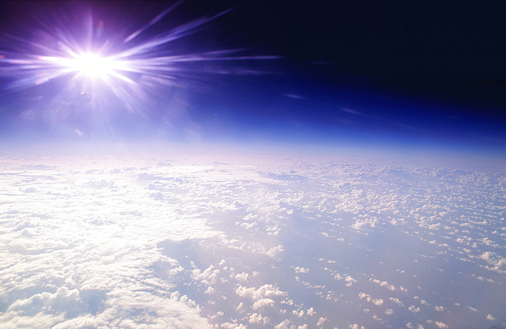 Aerial view over ocean and clouds, from high atmosphere, with distorted sun