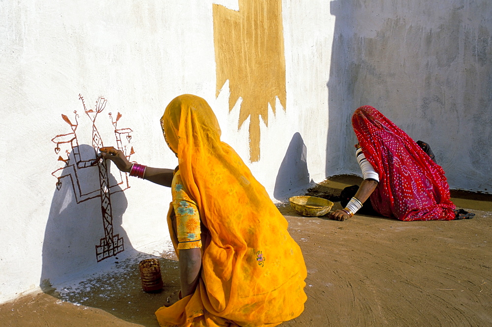 Women painting design on a wall in a village near Jaisalmer, Rajasthan state, India, Asia